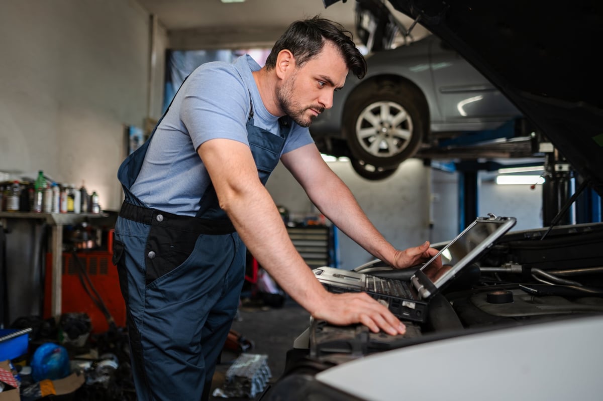 Mechanic using diagnostic software on a laptop to check a car engine in a garage