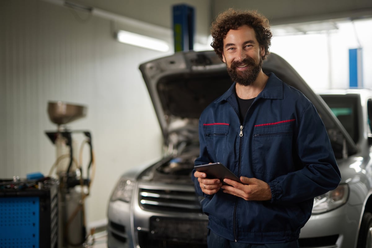 Portrait of a smiling car mechanic holding a tablet while working on a car in a repair shop