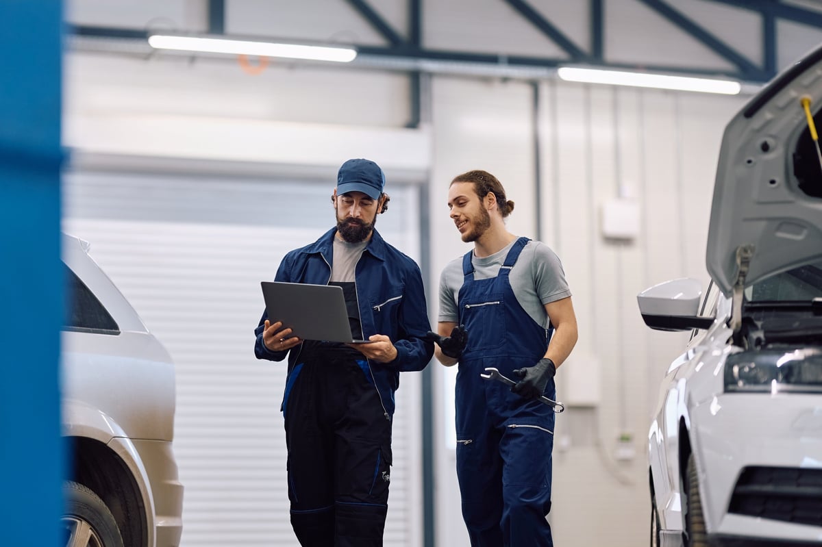 Mature mechanic and his younger coworker using laptop while working in auto repair shop