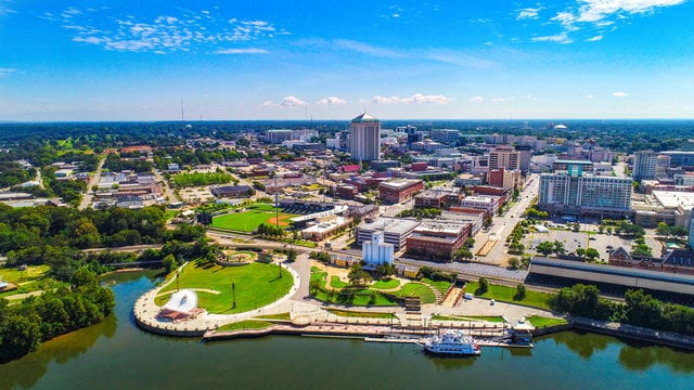 Aerial view of a riverfront city with parks, modern buildings, and blue sky