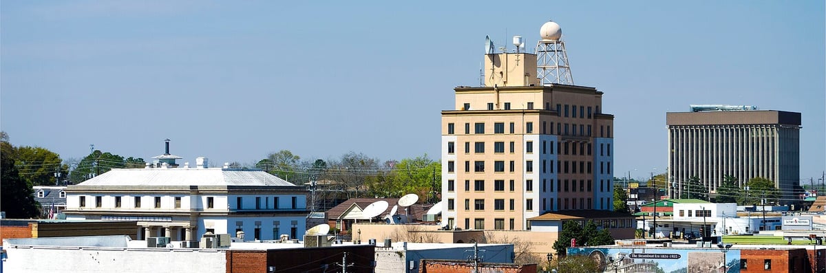 Industrial waterfront cityscape showing vintage and modern buildings including a tan art deco tower under blue sky