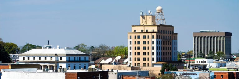 Industrial waterfront cityscape showing vintage and modern buildings including a tan art deco tower under blue sky
